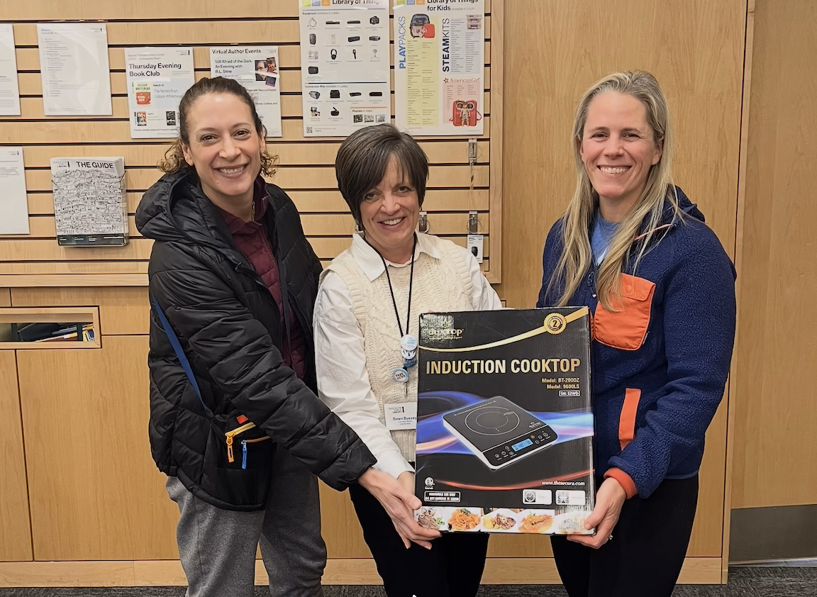 three women hold an induction burner box in the library